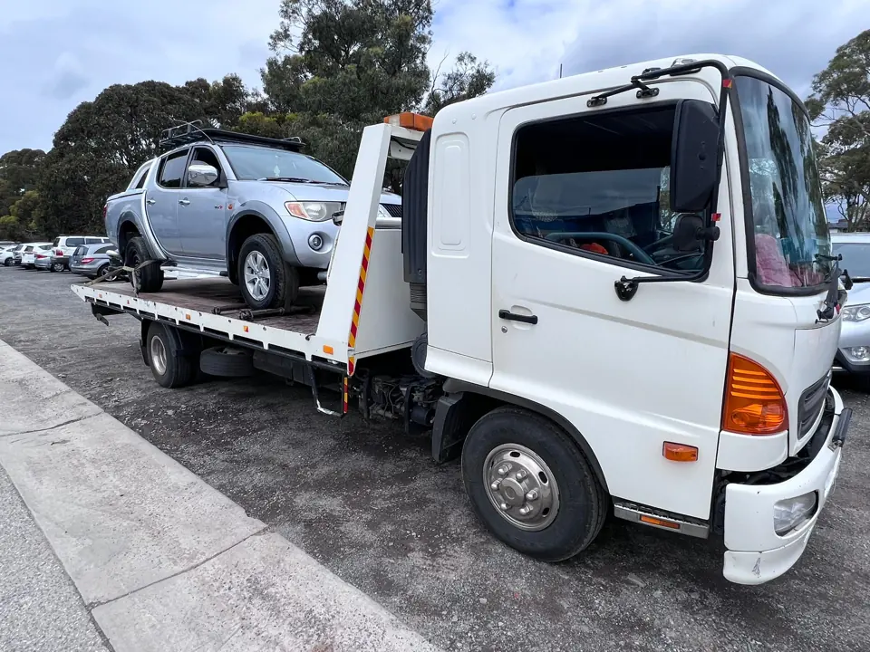 White flatbed truck carrying a silver vehicle